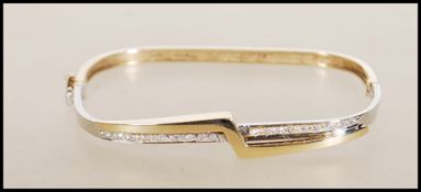 A hallmarked 9ct gold bangle of square form having a crossover of white and yellow gold, set with