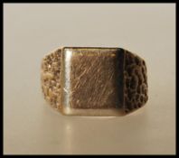 A hallmarked 9ct gold signet ring having a square unengraved head and bark effect shoulders.
