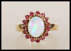 A stamped 9ct gold ring set with a central opal cabochon with a halo of red stones. Weight 4.7g.