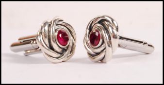 A pair of sterling silver knot design cufflinks set with central round cut rubies. Weight 12.8g.