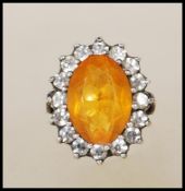 A stamped 9ct gold and silver ladies dress ring set with an oval cut orange stone with a halo of