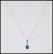 A stamped 18ct white gold necklace pendant having a central oval faceted cut emerald with a halo