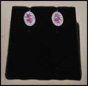 A pair of stamped 18ct white gold earrings having central faceted cut pink sapphires with a halo