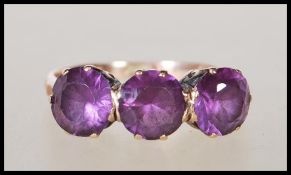 A stamped 9ct yellow gold ladies dress ring prong set with three purple stones on a decorative