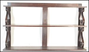 An early 20th Century mahogany graduating three tier wall hanging shelf rack having scroll side