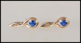 A pair of hallmarked 9ct gold earrings having a twist design set with two round cut sapphires.