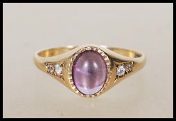 A 9ct gold English hallmarked ring set with a central purple cabochon stone flanked by two white