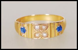 A hallmarked 15ct gold ring set with four seed pearls flanked by two gypsy set sapphires. Hallmarked