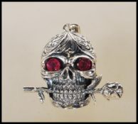 A stamped 925 silver pendant necklace in the form of a skull having ruby stone eyes and a rose in