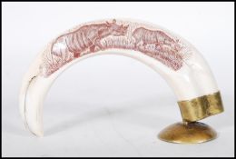 A 20th Century African warthog tusk supported by a brass base being engraved with rhinoceros