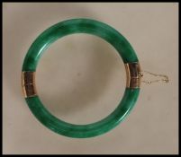An oriental gold mounted green jade hinged bangle with two hinged sections of green jadeite united
