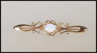 A hallmarked 9ct gold bar brooch having scrolled decoration set with a central opal cabochon.