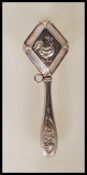 A continental silver baby's rattle of diamond shape form with central cockerel embossed decoration