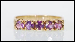 A hallmarked 9ct yellow gold ring set with five round cut purple stones with decorative scrolled