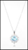 A silver drop pendant necklace set with a central faceted cut blue topaz having a halo of white