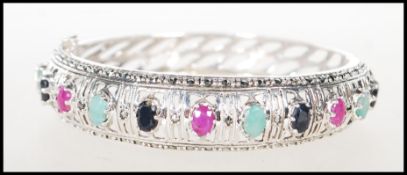 An impressive silver bangle having pierced decoration around with prong set ruby, sapphire and green