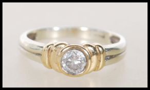 A 9ct two tone gold diamond solitaire ring having a bezel set brilliant cut diamond on a reeded