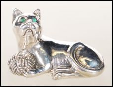 A stamped 925 sterling silver figure of a seated cat playing with a ball of wool set with green