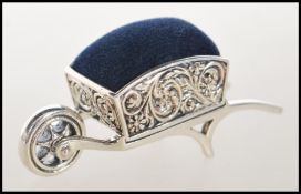 A stamped sterling silver pincushion in the from of wheelbarrow having embossed swirl and floral