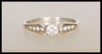 A stamped 375 9ct white gold ring set with a central round cut stone with accent stones to the