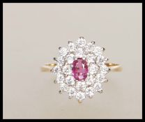An English hallmarked ladies cluster ring set with a central oval cut red stone with a cluster of