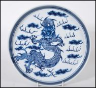 A 19th Century Chinese ceramic plate being hand painted in blue depicting a five toed dragon to