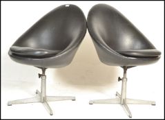 A pair of contemporary retro style swivel tub chairs, upholstered in a black leatherette material