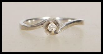 A stamped 375 white gold solitaire ring of cross over design set with a round cut white stone.