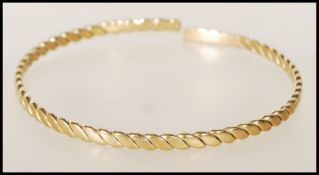 A 20th century stamped 9ct yellow gold bangle bracelet of twisted form, having an opening to the