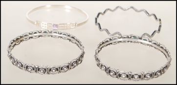A group of four silver bangle bracelets to include a stamped 925 wave design bangle, a stamped 925