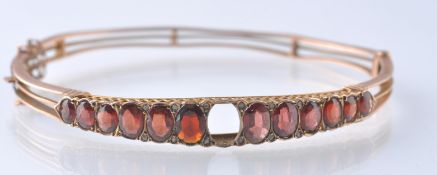 AN EARLY 20TH CENTURY HALLMARKED 9CT GOLD GARNET AND DIAMOND HINGED BANGLE