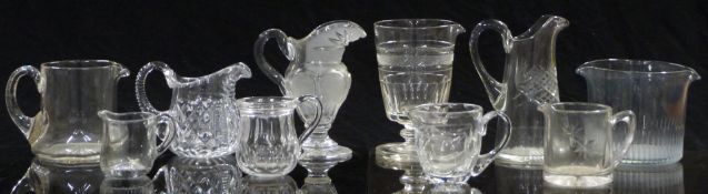 Ten various clear glass jugs and measures most with cut decoration, largest 15.5cm tall.
