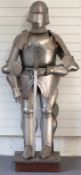 A replica suit of armour and sword on plinth including gorget, visor, breastplate, fan plate, grieve