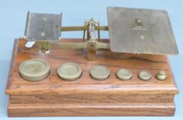 Victorian brass postage scales on oak base with weights from 8oz to 1/2oz, width 29cm