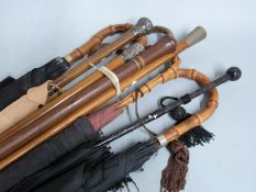 A collection of walking sticks, umbrellas and parasols including two with hallmarked silver mounts/