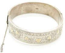 A silver bangle with engraved decoration and applied gold detail
