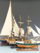 Three wooden model ships comprising a sailing yacht, galleon and a trawler, all on wooden stands,