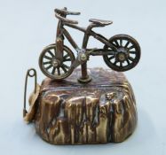 Novelty sewing tape measure formed as a bicycle on rock, the bicycle turning to retract the tape,