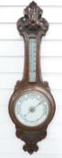 A early 20thC carved oak aneroid barometer, the white enamelled dial with bold black predictions,