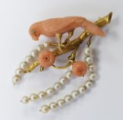 An 18ct gold brooch in the form of a parrot on a branch, the parrot of carved coral set with a