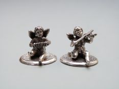 A pair of white metal novelty menu holders with cherubs playing instruments, both stamped 925,