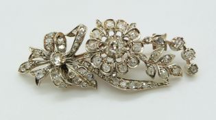 An early 20thC gold brooch set with diamonds in a floral, bow and foliate design, 6cm long