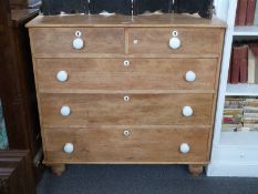 A pine chest of two over three graduated drawers with white ceramic handles, raised on carved