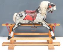 A carved dapple grey rocking horse on pine base with padded saddle and leather truck, height 93cm,