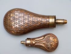 Two copper and brass powder flasks with embossed decoration, largest 18.5cm long.