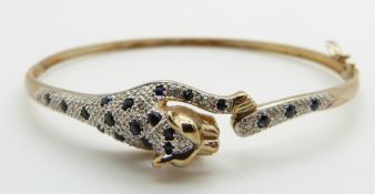 A 9ct gold bangle depicting a leopard set with sapphires and diamonds, 8.6g, 6 x 5.4cm