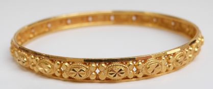 A yellow metal bangle with raised decoration marked 22ct gold, 17.6g (6.5 x 6.3cm)