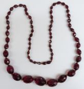 A cherry amber necklace of 65 graduated faceted oval beads, the largest 26.7x21.7mm, 68g.