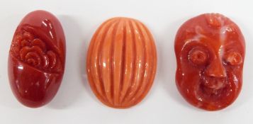 A carved coral head of a laughing man and two carved coral beads