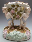 German figural porcelain oil lamp supported by four putti and decorated with applied flowers, blue